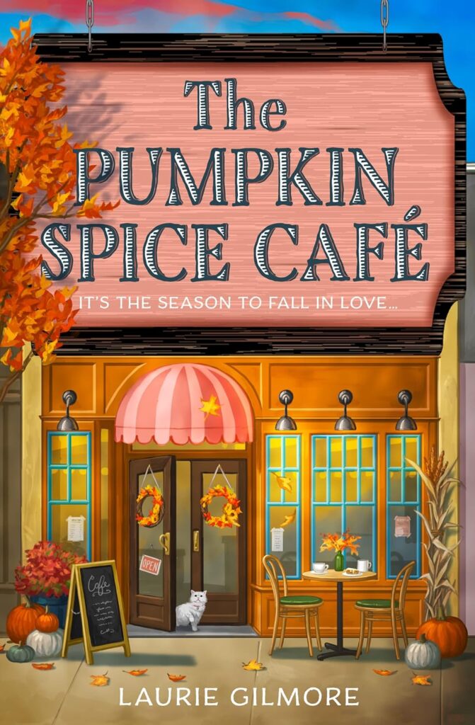Cover of The Pumpkin Spice Cafe. The title is on a sign over a storefront. The cafe has an orangey-pink striped awning over the door, big, windows, fall wreaths on the doors, a sandwich board outside the doors, and a two-person table in front of the windows with a fall bouquet, two cups of coffee, and a pastry. There is a white cat coming out of the door.