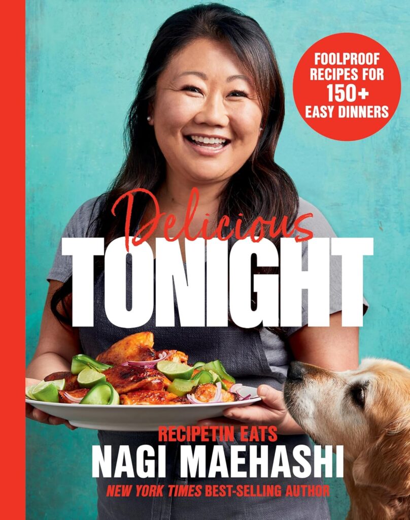 Cover of Delicious Tonight. Author Nagi Maehashi is holding a dish from her cookbook, and her dog's nose is right beside the plate, ready to eat. She is smiling and offering the food to the reader.