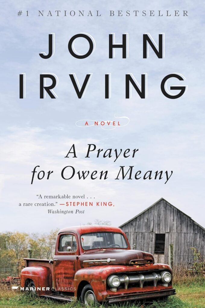 Cover of A Prayer for Owen Meany. The foreground has an old red truck parked in front of a barn/shed. Most of the background is blue sky with some wispy white clouds.