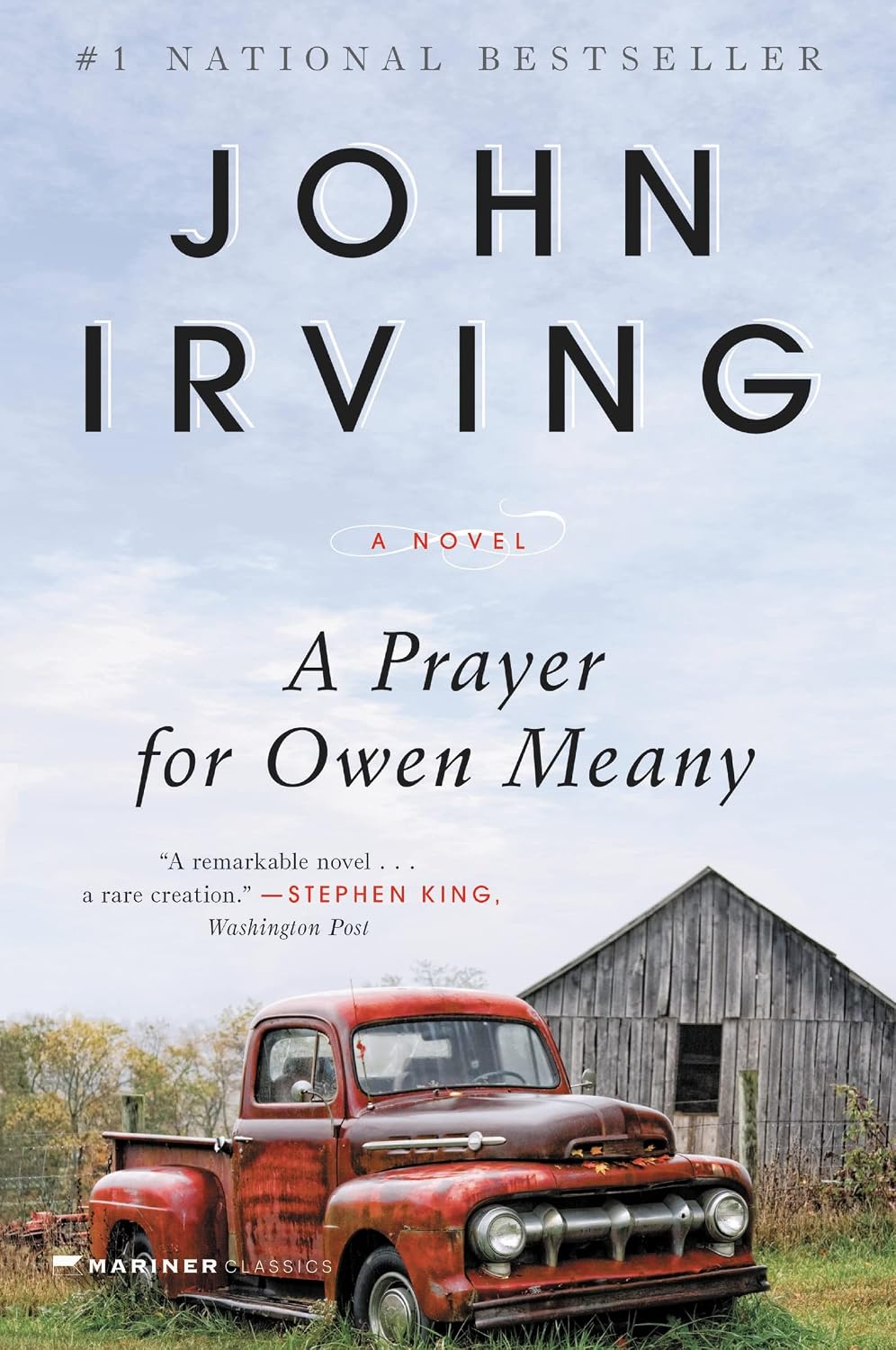 Cover of A Prayer for Owen Meany. The foreground has an old red truck parked in front of a barn/shed. Most of the background is blue sky with some wispy white clouds.