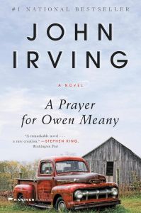 Cover of A Prayer for Owen Meany. The foreground has an old red truck parked in front of a barn/shed. Most of the background is blue sky with some wispy white clouds.
